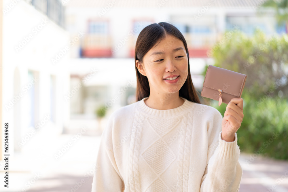 Pretty Chinese woman holding a wallet at outdoors with happy expression Pretty Chinese woman holding a wallet at outdoors with happy expression