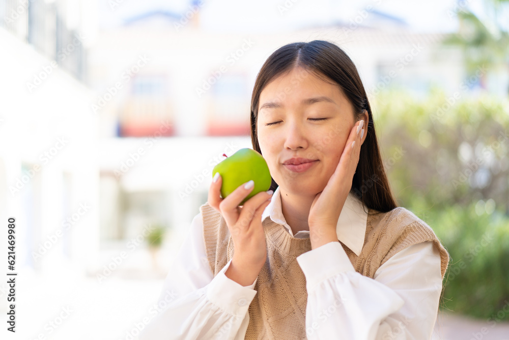 Pretty Chinese woman at outdoors holding an apple with happy expression Pretty Chinese woman at outdoors holding an apple with happy expression