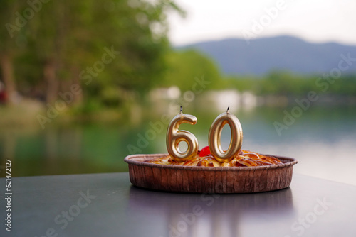 anniversary of 60 year old person with golden candles on a cake outside. birthday celebration of a mature person