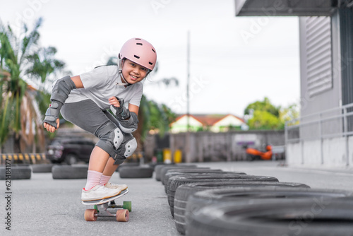 asian child skater or kid girl fun playing skateboard or smile riding carving surf skate on car tires track in skatepark lane for extreme sports exercise and wears helmet knee guard for body safety