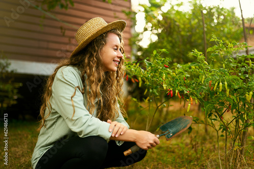 Young female gardener smiles on her farm sitting among plants. Happy cauasian woman in her garden with a scoop near ripe harvest of vegetables. Farming and gardening concept photo
