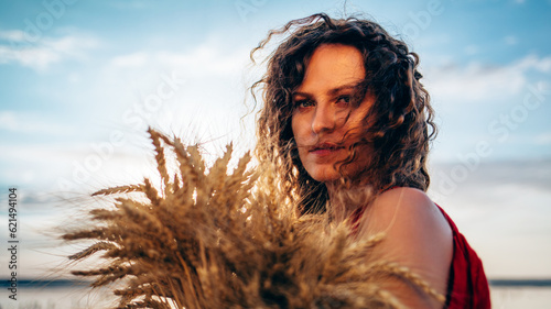 A curly girl in a red dress with ears of wheat in her hands