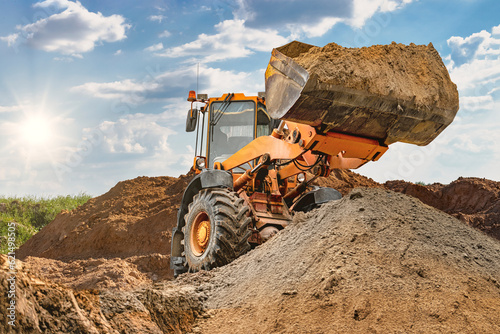 Wheel front loader bulldozer pours sand. Distributes sand for road construction. Powerful earthmoving equipment. Construction site. Rental of construction equipment.