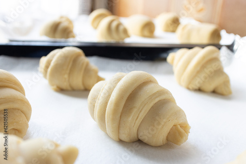 Close up of layered of several fluffy leavened uncooked traditional French croissants dough in a baking tray over paper sheet before put in oven. It's a buttery, flaky pastry of Austrian