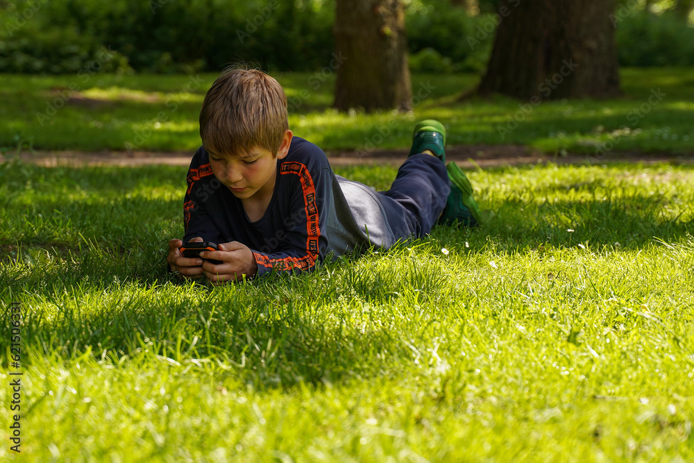 A teenager on the grass, bent over the phone, the problem of children's gambling addiction. A teenager on the grass, bent over the phone, the problem of children's gambling addiction.