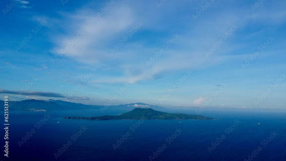 Tropical island in the middle of the sea. Aerial view of a green tropical island on the horizon surrounded by blue sea.