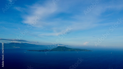 Tropical island in the middle of the sea. Aerial view of a green tropical island on the horizon surrounded by blue sea. © Houston