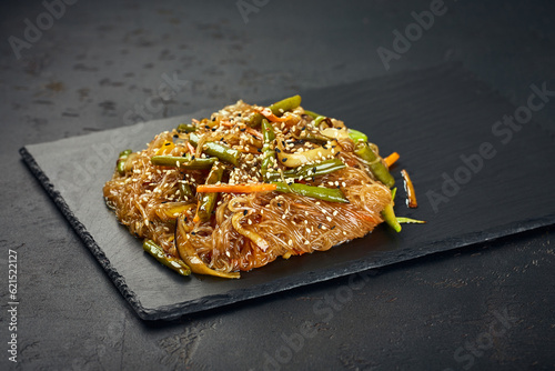 Asian glass udon noodles with vegetables and sesame seeds on dark background