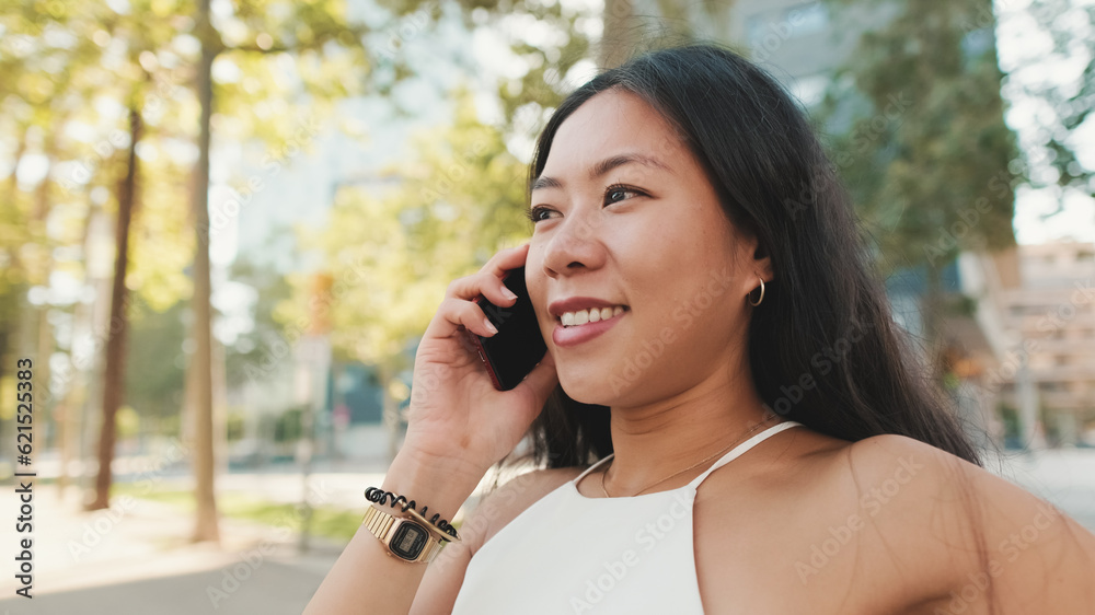 Cute brunette girl, dressed in white top and jeans, sits on bench on cityscape background, talking on smartphone Cute brunette girl, dressed in white top and jeans, sits on bench on cityscape background, talking on smartphone