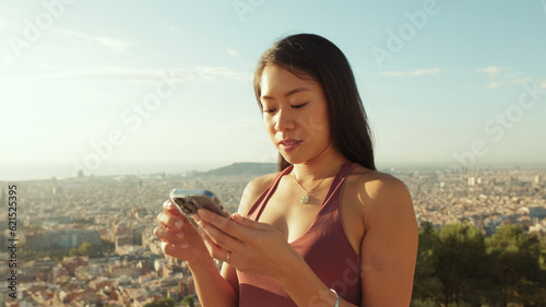 Close up, happy athletic woman using mobile phone while standing at lookout point, Backlighting
