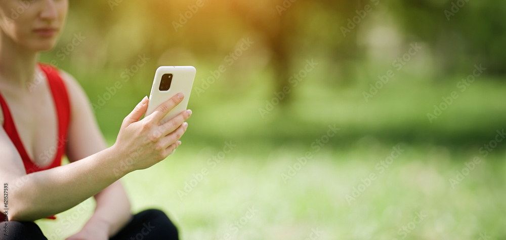Young woman using smartphone after doing yoga outdoors in the park, sports yoga concept    