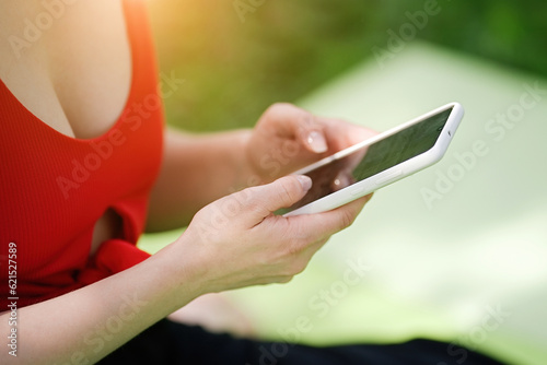 Young woman using smartphone after doing yoga outdoors in the park, sports yoga concept 