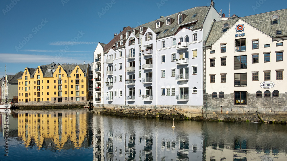 Lined up symmetrical townhouses and buildings with the crisp reflection of their architecture in the clean waters of the canal passing through the quaint coastal town in Alesund, Norway