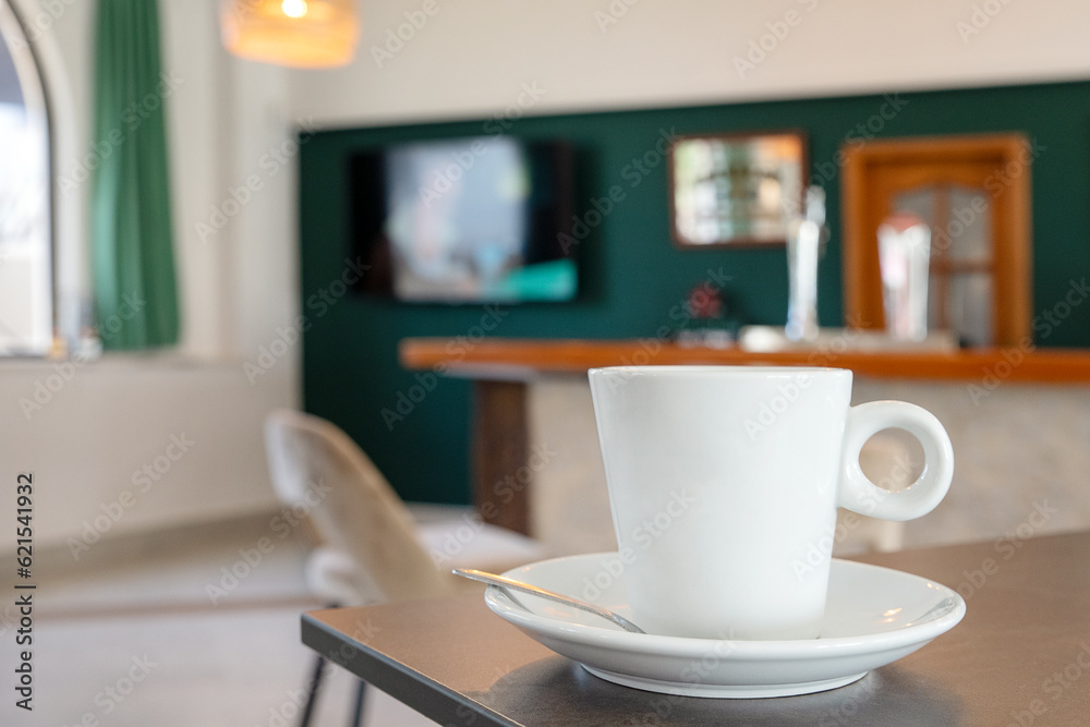 Comfortable interior of a bar or cafe with focus on a cup of hot beverage, coffee or tea resting on a high table, cozy atmosphere for having a drink, working remotely or supporting a local business Comfortable interior of a bar or cafe with focus on a cup of hot beverage, coffee or tea resting on a high table, cozy atmosphere for having a drink, working remotely or supporting a local business