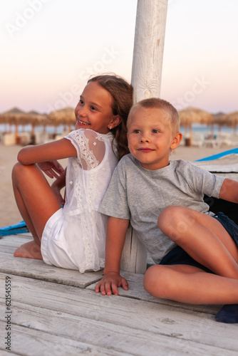  brother and sister are sitting at sunset on the beach at the boat. the chilfren look forward an smiles.   photo