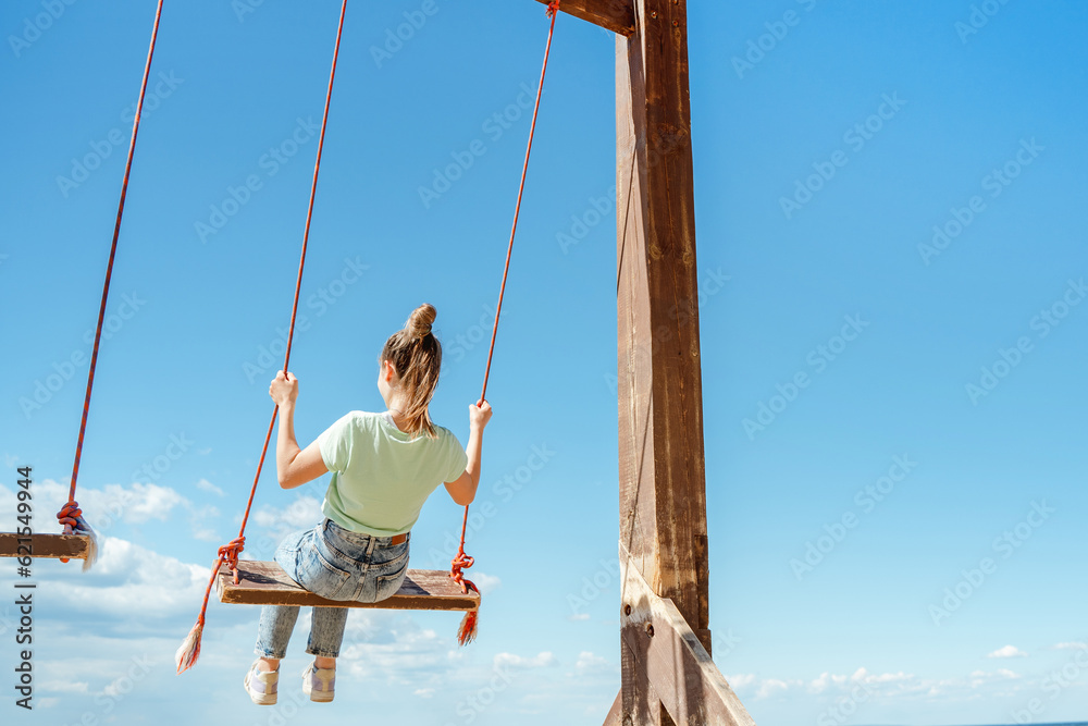 A teenage girl in jeans rides on a swing on the seashore on the beach