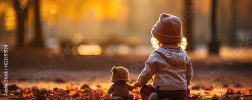 Little girl with her friend bear playing with autumn leaves in the park