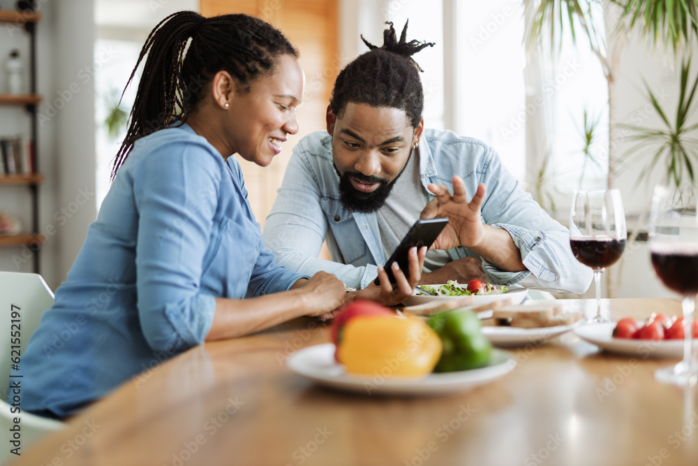 Happy African American couple using a phone while having breakfast in the morning