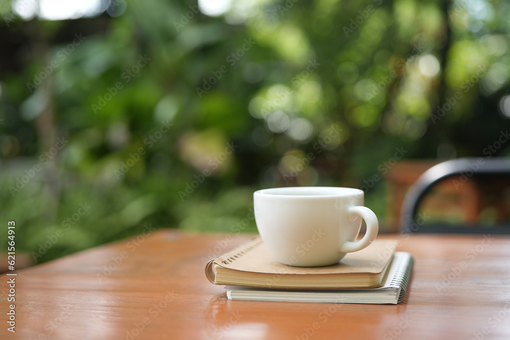 White coffee cup and bronze spoon on brown wooden table with green lush background White coffee cup and bronze spoon on brown wooden table with green lush background