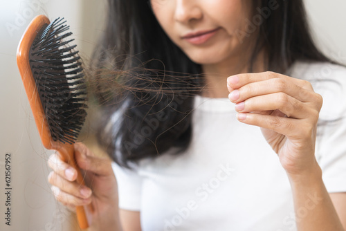 Murais de parede Serious asian young woman holding brush holding comb, hairbrush with fall black hair from scalp after brushing, looking on hand worry about balding