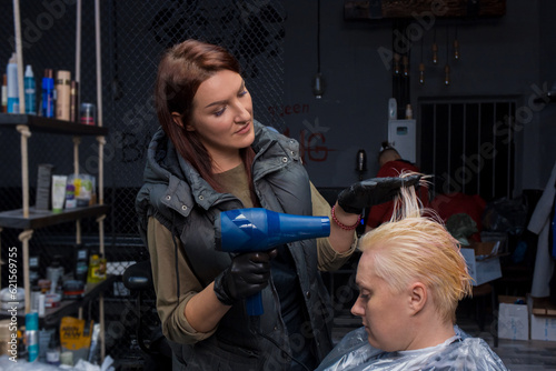 A sweet, kind brunette girl, a professional barbershop in the process of work, dries the client's hair