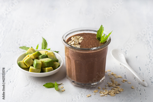 Chocolate smoothie or cocktail with frozen avocado and oatmeal garnished with mint leaves on a light blue table. vegan food