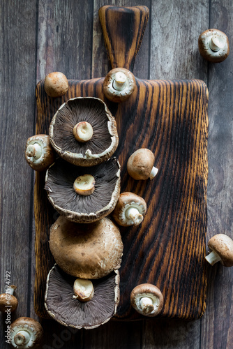 Portobello and cremini mushrooms on a dark wooden board.