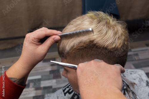 The hands of a salon worker with scissors and a comb cut the hair of a client, a barbershop guy, hairdressing services