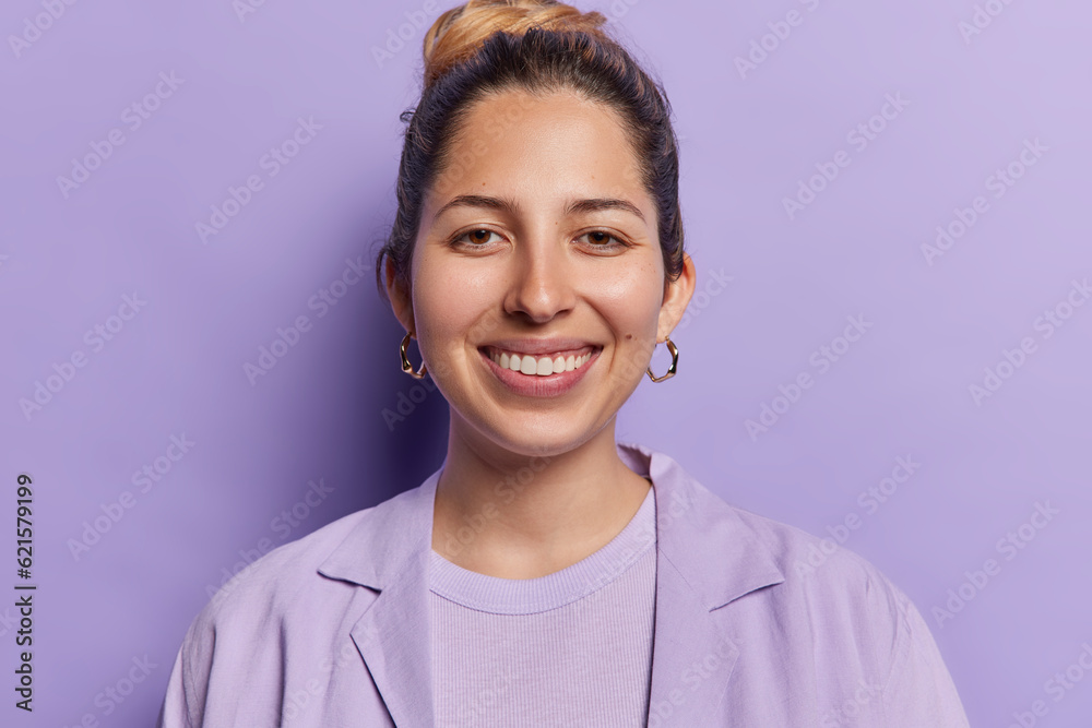 Portrait of cheerful young European woman with combed hair smiles toothily looks directly at camera dressed in shirt expresses positive emotions isolated over purple background happy to be promoted Portrait of cheerful young European woman with combed hair smiles toothily looks directly at camera dressed in shirt expresses positive emotions isolated over purple background happy to be promoted