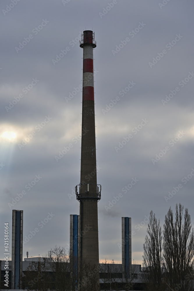 Industrial buildings and old disused chimney with mobile antennas on cloudy sky background.