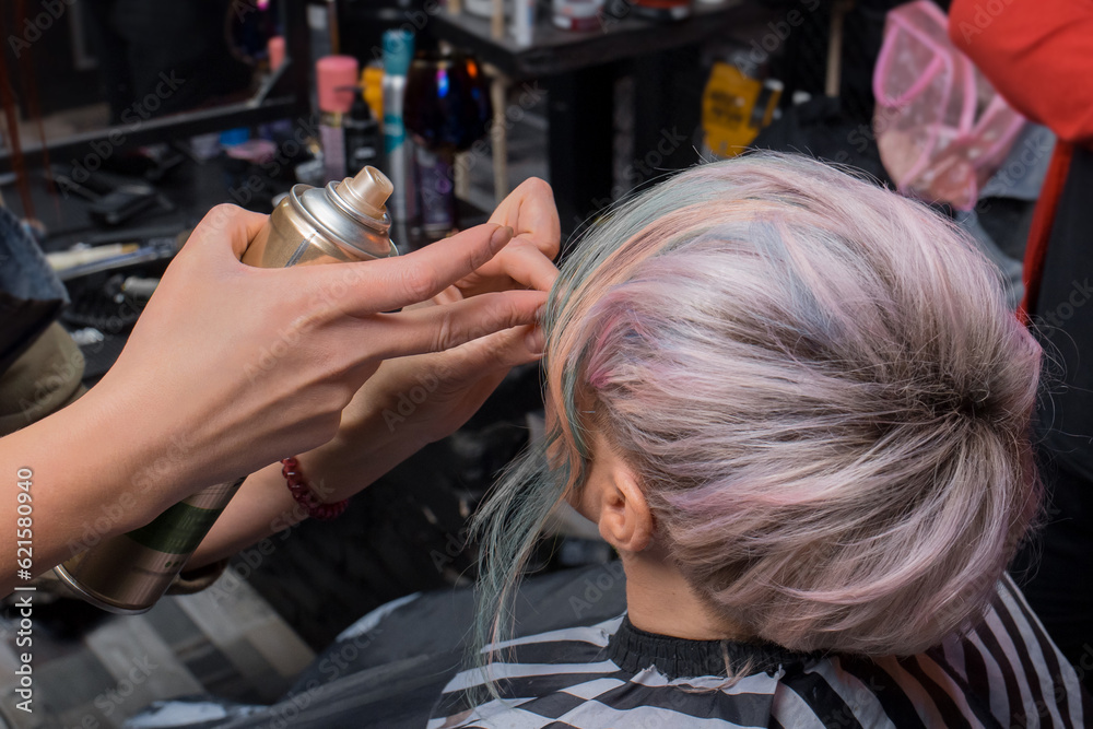 Fototapeta premium The girl's hands of a professional hairdresser-stylist-make-up artist hold the varnish and straighten the hair of a stylish, fashionable hairstyle color coloring creative bob