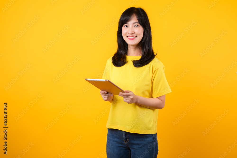 Experience the joy of education technology with portrait. A young Asian woman wearing a yellow t-shirt and denim jeans showcases a happy smile while using digital tablet. education technology concept. Experience the joy of education technology with portrait. A young Asian woman wearing a yellow t-shirt and denim jeans showcases a happy smile while using digital tablet. education technology concept.