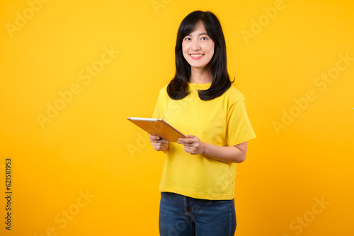 Experience the joy of education technology with portrait. A young Asian woman wearing a yellow t-shirt and denim jeans showcases a happy smile while using digital tablet. education technology concept.