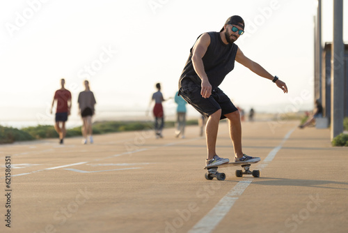 Adult attractive man in black clothes skating on the street by the beach