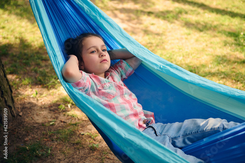 Beautiful little child girl relaxing outdoors, lying on a hammock on a sunny summer day. Childhood. Recreation. Holidays
