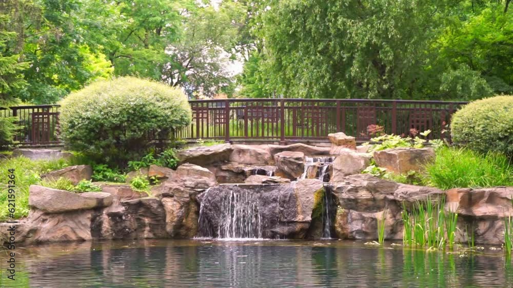 Small decorative waterfall with stones in a public park or garden in summer day. Landscape design, decor. Small decorative waterfall with stones in a public park or garden in summer day. Landscape design, decor.