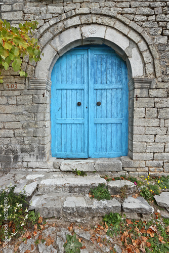 Exquisite blue wooden door of a entirely stone-built house with an apotropaic symbol above the door. Found in the village of Kalarrytes, in the mountainous region of Tzoumerka, in Greece, Europe.