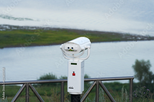 Viewing binoculars on a platform on the high bank of a picturesque river. Copy space