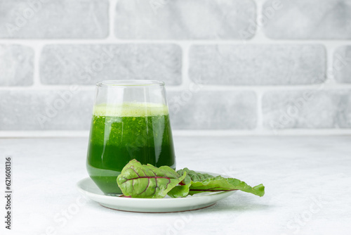 Freshly squeezed juice or smoothie in a glass with fresh chard leaves  on plate on a light table with copy space