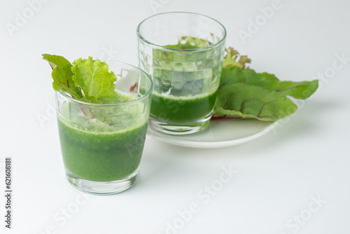 Two glasses with freshly squeezed juice or smoothie with fresh  chard leaves on on a white background with copy space