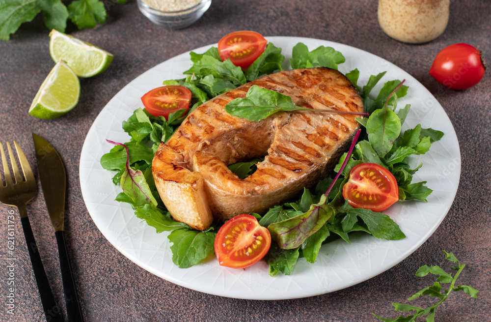 Baked salmon steak served with arugula and cherry tomatoes on a white plate