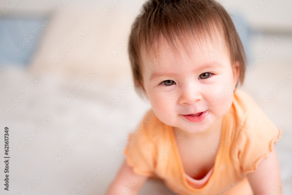 lifestyle home portrait of happy and adorable 9 months old baby girl looking at the camera in funny face expression on white background crawling on bed