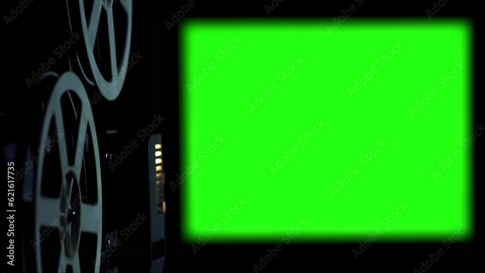 Old Cinema Projector Displays Green Screen. In a dark room you can see parts of the film projector and his wheels that turn.