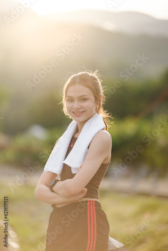 Portrait young attractive smiling fit woman with white towel resting after workout exercises outdoors on a background of park trees. Healthy lifestyle wellness happiness concept.