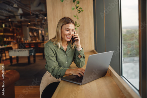 Woman entrepreneur is talking phone in coworking during work on laptop. Distance work concept