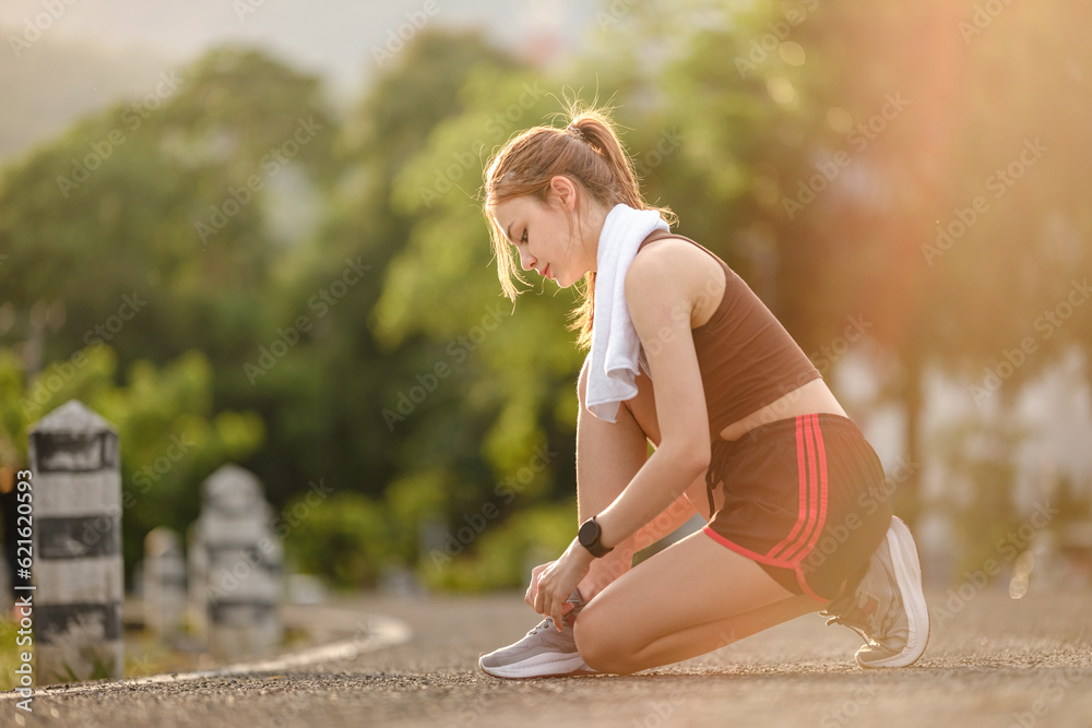 Female runner kneeling and tying shoelace on the street. Fitness woman tying shoelaces. Young woman runner tying shoelaces in park with sunset and sunbeam.