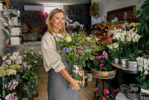 Obraz na plátne Attractive woman flower shop owner in apron holding bouquet of flowers at floris