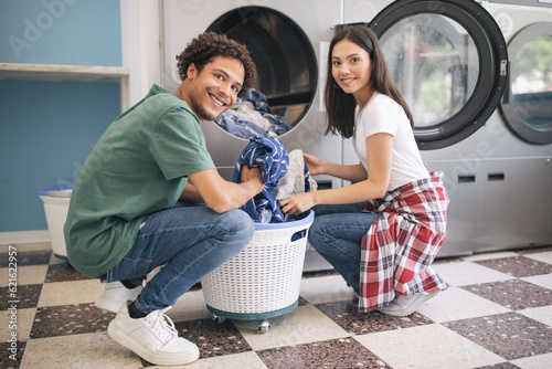 Slika na platnu Happy Couple Doing Laundry Loading Washer Machine At Laundromat Room