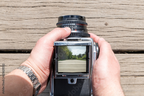 A man takes a photo of a path through nature with a vintage viewfinder camera.