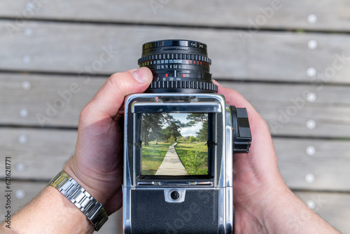 A man takes a photo of a path through nature with a vintage viewfinder camera.